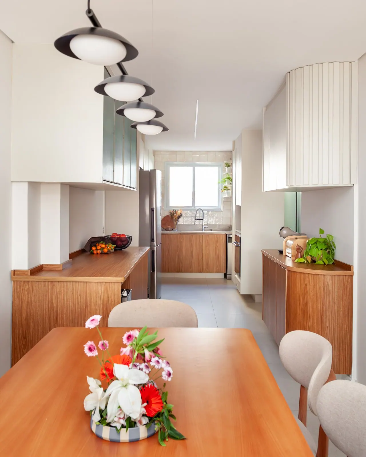 Sala de jantar com mesa de madeira e pendentes pretos em apartamento em São Caetano do Sul