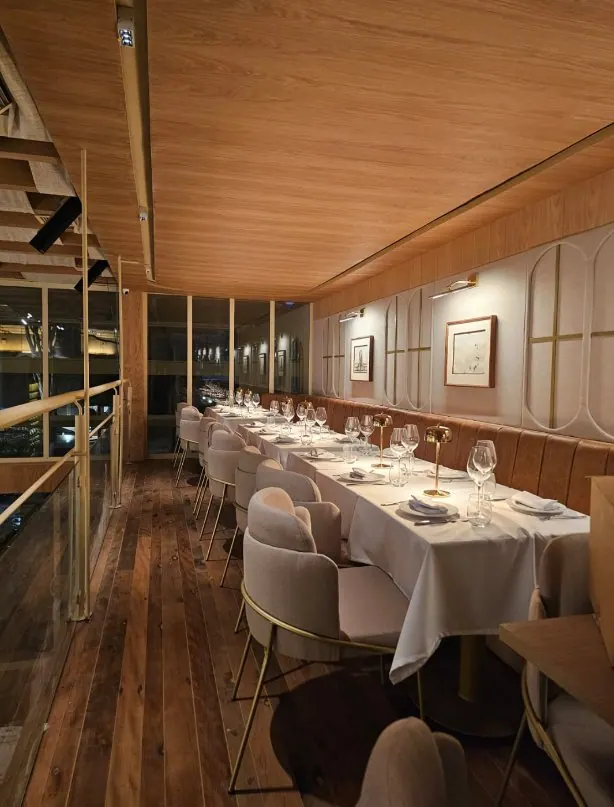 Mesa longa de restaurante junto à janela com forro de madeira iluminado