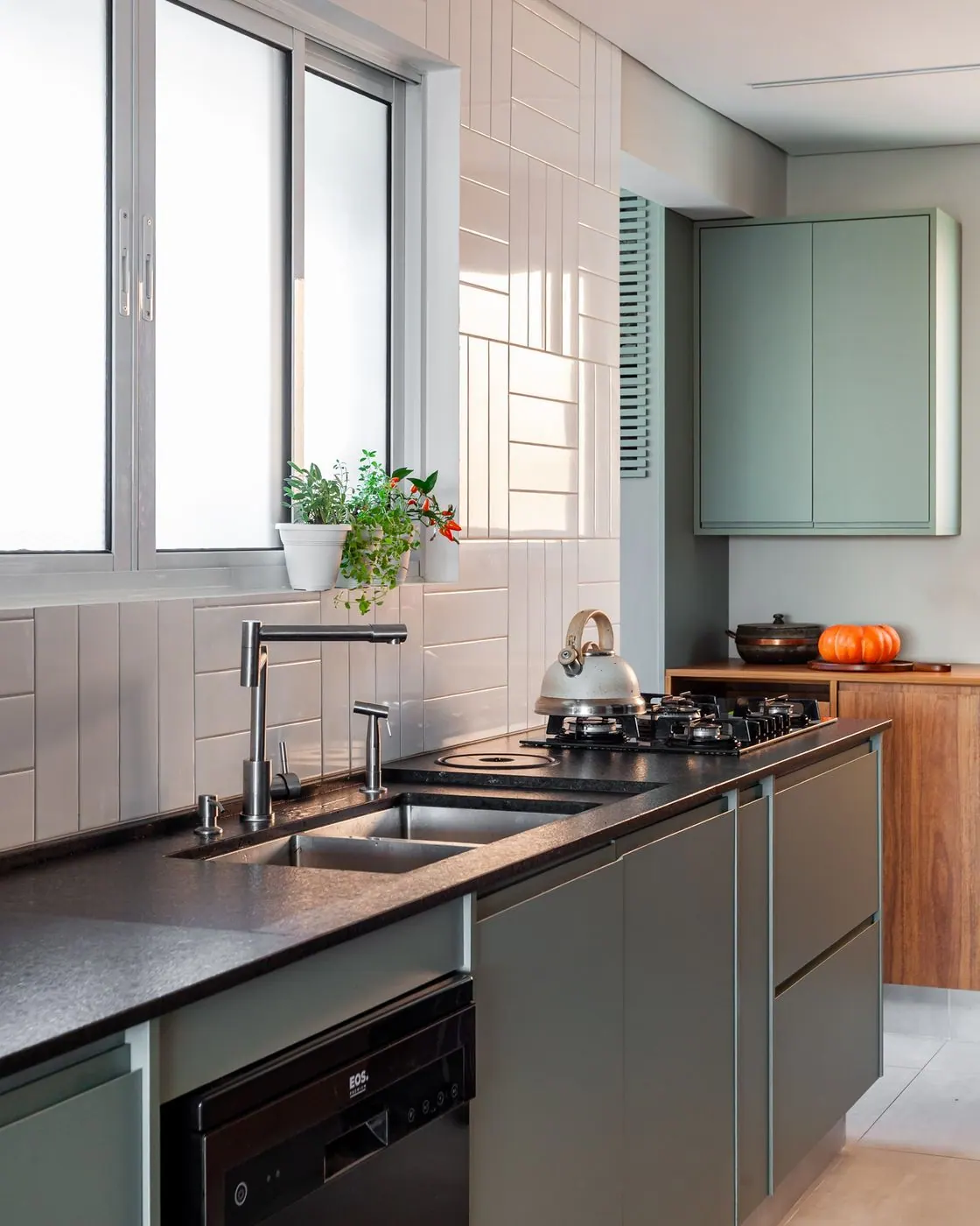 Bancada preta com armários verdes e revestimento branco na cozinha
