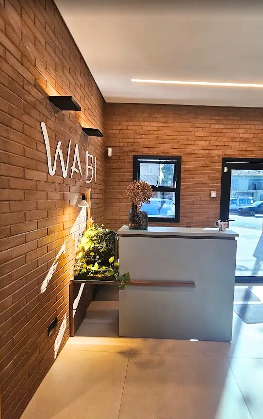 Balcão de recepção com letreiro Wabi iluminado e parede de tijolinho